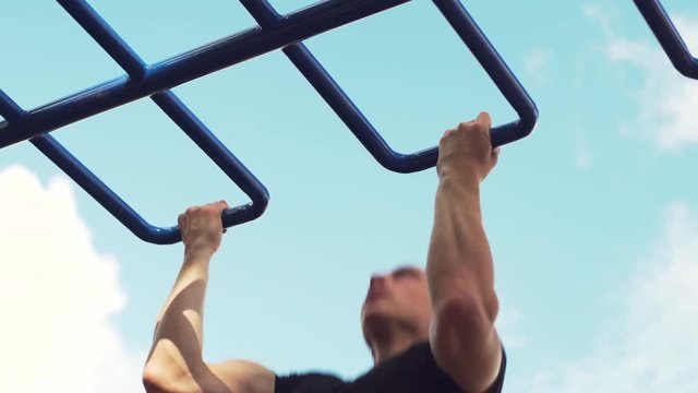 Young Strong Man Is Engaged in Street Workout. Male Athlete Doing Pull Ups on Parallel Bars. Summer Training in Park