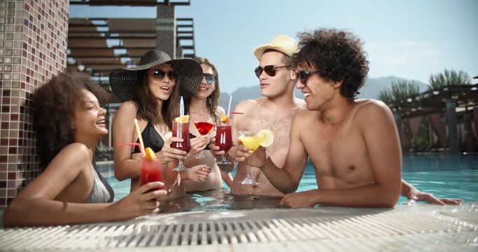 Group of multiethnic friends enjoying theit time in swimming pool, chatting and drinking cocktails. Vacation concept 4k