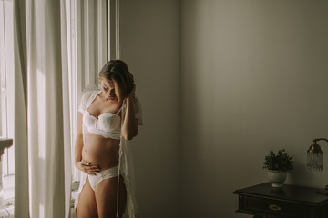 Young pregnant woman standing by the window