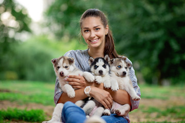 A beautiful smiling woman with a ponytail and wearing a striped shirt is holding three sweet husky puppies on the lawn. Love and care for pets.