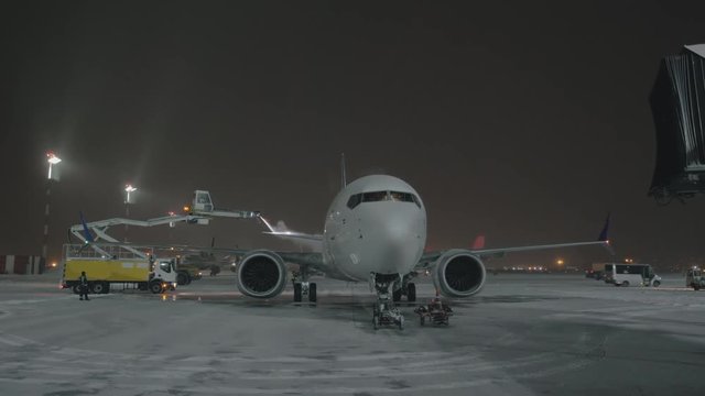 Airport staff preparing airplane for the flight and de-icing tail wing of the aircraft, view at winter night