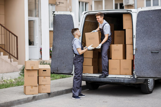 Two young handsome movers wearing uniforms are unloading the van