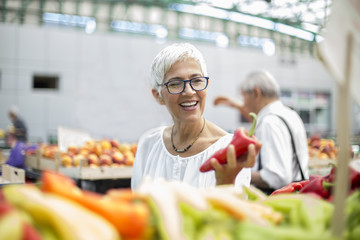 Good-looking senior woman wearing glasses buys pepper on market