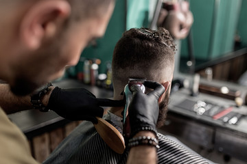 Barber in black gloves shaves man's hairs at the back at a barber shop.