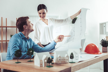 Obraz premium Show it to me. Amazing woman standing near her colleague and holding sketch in hands