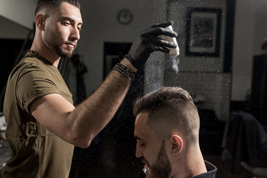 Handsome barber is fixing the styling of brutal young man with a dry styler at a barbershop