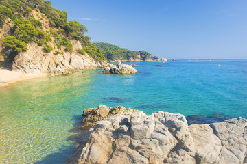 Marine tropical lagoon. Turquoise water on beach with white sand and rocks along coastline. Beaches of Lloret de Mar, Costa Brava, Spain. Clear summer day at sea. Nature of Mediterranean.