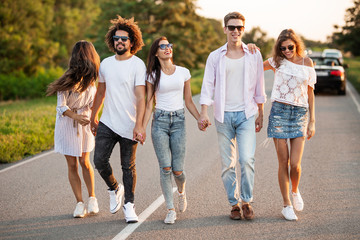 Young happy guys and girls are  holding hands and walking on the road on a sunny day