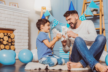 Men games. Joyful appealing man playing with toy while celebrating birthday with son