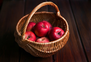Red apples in a wicker basket on dark wooden boards