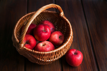 Red apples in a wicker basket on dark wooden boards