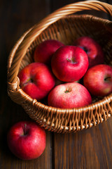 Red apples in a wicker basket on dark wooden boards