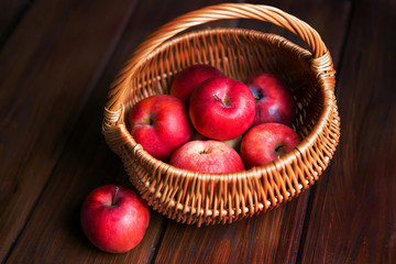 Red apples in a wicker basket on dark wooden boards