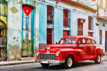 Gordijnen Klassieke auto en en oud gebouw met de Cubaanse vlag in Oud Havana © kmiragaya