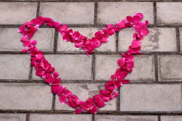 Red heart of rose petals laid out on the tile, wall.