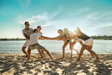 Friends funny tug of war on the beach under sunset sunlight in sun
