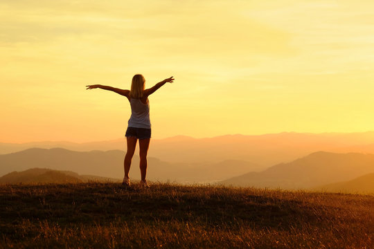 Happy woman with open arms stay on the peak of the mountain top