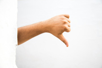 male adult hand showing thumbs down gesture from behind a wall