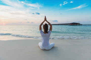 Back of views Asian woman wearing white sportswear practicing yoga Lotus pose on the beach in...