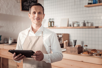 Business owner. Serious smart man holding a tablet while looking at you