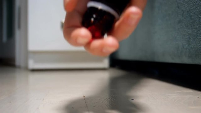 Closeup video of female hand holding bottle of pills slowly falling on floor at bedroom. Concept of medicines overdose or suicide