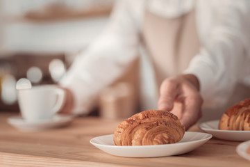 In the bakery. Selective focus of a tasty croissant being taken by a professional skilled waiter