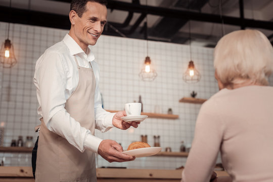 Coffee and croissant. Cheerful nice man smiling while bringing breakfast to the customer