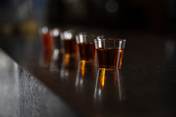 Line of whiskey shots with their reflection on a black bar in a dark room