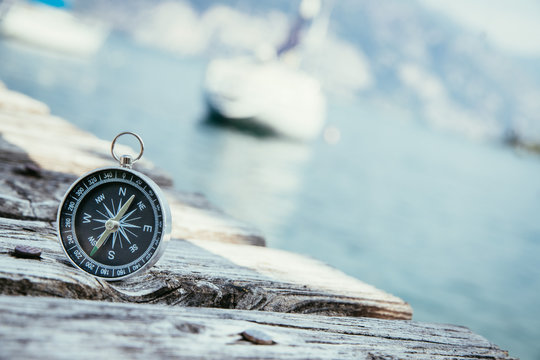 Kompass auf Holzplanken eines Steges, Boot im Hintergrund, Business