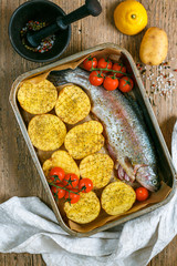 Raw salmon (trout) is ready for baking with vegetables-potatoes, onions, tomatoes and spices. Cooking a delicious healthy dinner. Rustic style