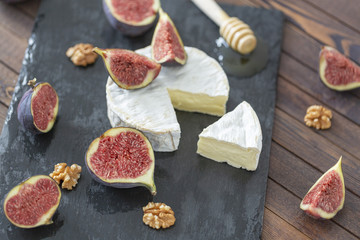 Brie cheese with fresh figs, honey and nuts. On shale plate and wooden background.