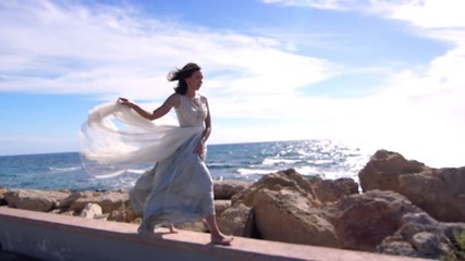 Elegant woman in dress walking on stone beach. Cheerful woman enjoy summer walk in slow motion. Fashion model in elegant dress walking beach boardwalk. Summer model enjoy sea landscape