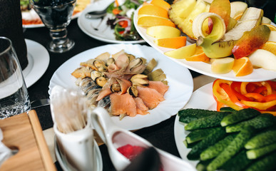 Set table with plates and dishes at the restaurant. Birthday party or wedding celebration at the cafe with different food. Black napkins and leather chairs. Fruit, fish and vegetable plates.