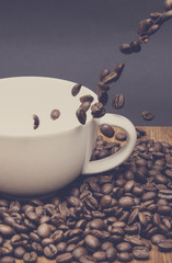 Coffee beans with a cup. Image has a vintage effect applied. Beans are poured to a white cup. Concept image.