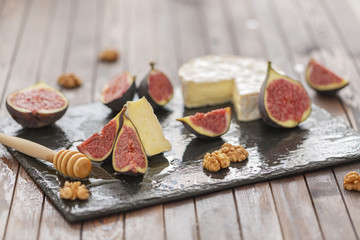 Brie cheese with fresh figs, honey and nuts. On shale plate and wooden background.