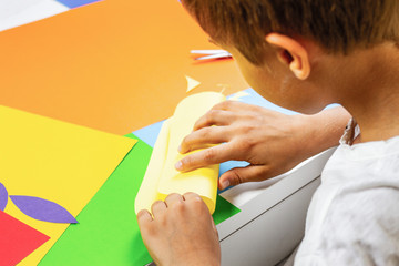 Child making greeting card with colored paper at the table