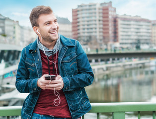 Satisfied young man listening to tracks and texting friends using cell phone