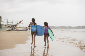 Rear view of two mixed-race sisters walking down the beach on a bright tropical summer holiday...