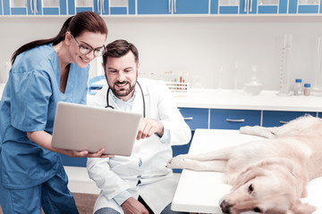 Modern technologies. Beautiful girl wearing medical uniform and bowing head while talking to her colleague