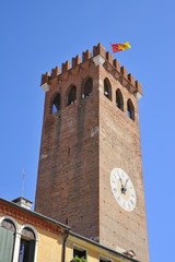 Antico campanile in mattoni di terracotta con orologio con le lancette e bandiera che sventola
