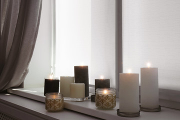 Burning candles on window sill in room