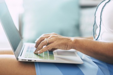 close up of bright and light woman hands typing and writing on a coloured keyboard on a notebook computer laptop. blue colors an window light at home like an alternative office and place to work