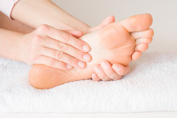 Groomed woman's hands doing massage. Barefoot on the white towel. Relaxing day. Body care concept.