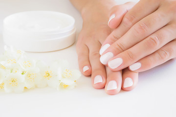 Young, perfect, groomed woman's hands using moisturizing, natural herbal cream. Care about nails and clean, soft, smooth skin in summer time. Beautiful jasmine blossoms. Fresh, white flowers.