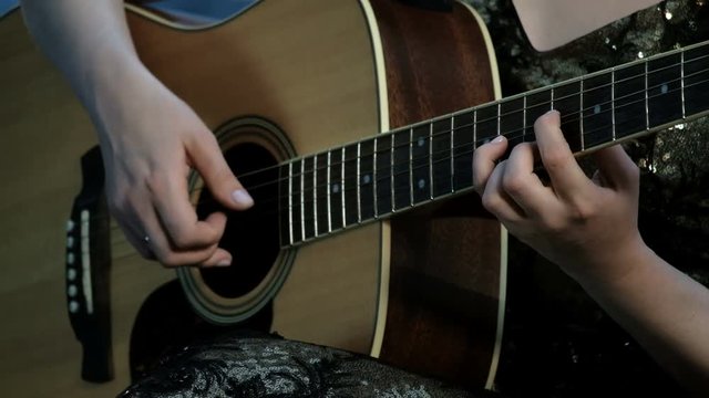 Close-up of the hands of a girl playing an acoustic guitar. Focus on the fingers clamping the chords on the fretboard. Day of music.