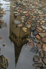 The bell tower of the Church of Sant Olav reflected in a puddle of water in the old town of...
