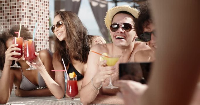Guy filming a video of his friends in swimming pool drinking cocktails and chatting. always online 4k