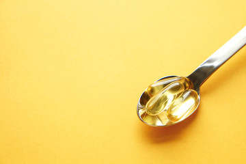 Bunch of omega 3 fish liver oil capsules in silver spoon. Close up of big golden translucent pills in pile. Healthy every day fatty acids nutritional supplement dosage. Top view, flat lay, copy space.