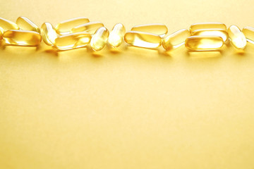 Bunch of omega 3 fish liver oil capsules in row forming pattern background. Close up of big golden translucent pills texture. Healthy every day nutritional supplement. Top view, flat lay, copy space.