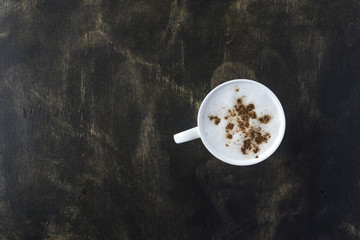 A cup of cappuccino coffee on a black wooden table. View from above. Free place for the inscription.